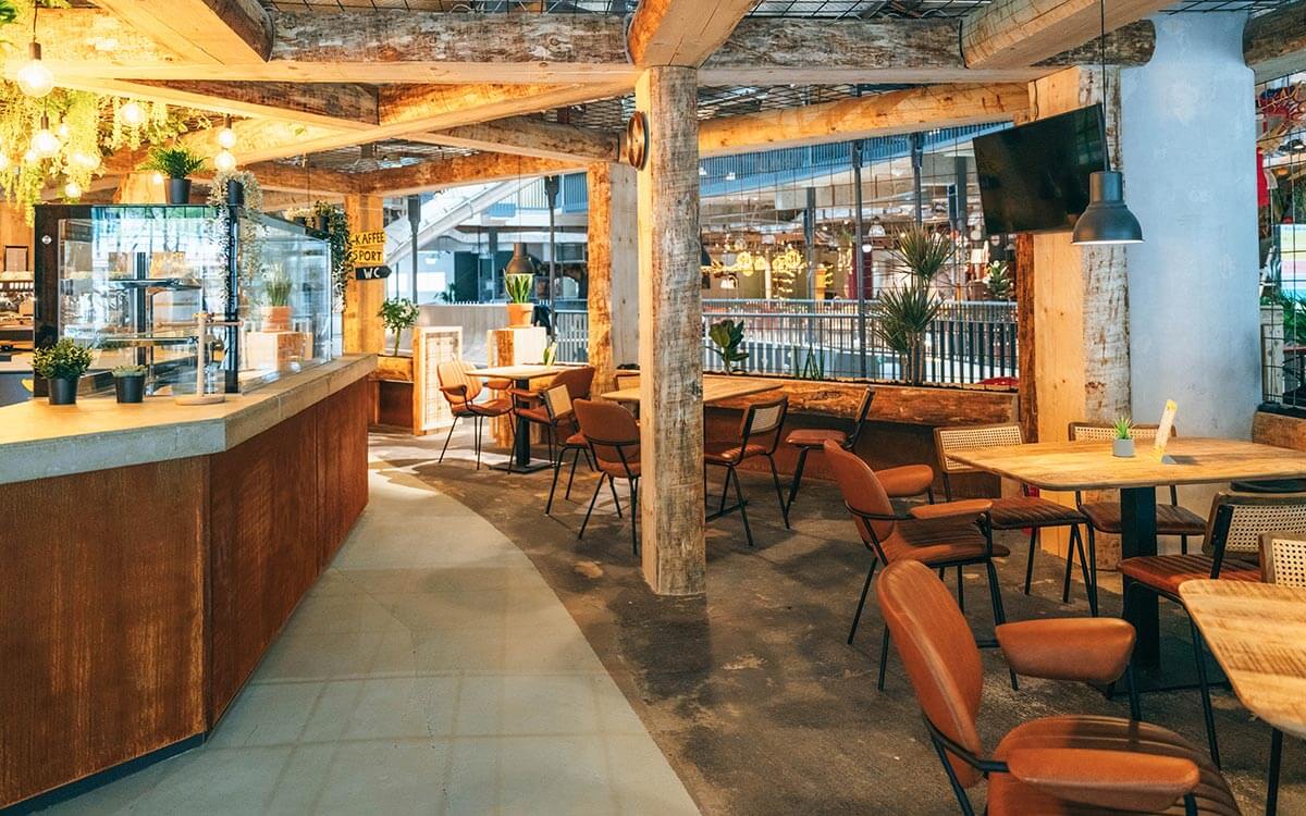 Gemütliches Bistro im Stuntwerk Troisdorf mit Holzelementen, warmem Licht, Pflanzen und modernen Sitzplätzen. Ideal zum Entspannen nach dem Training.
