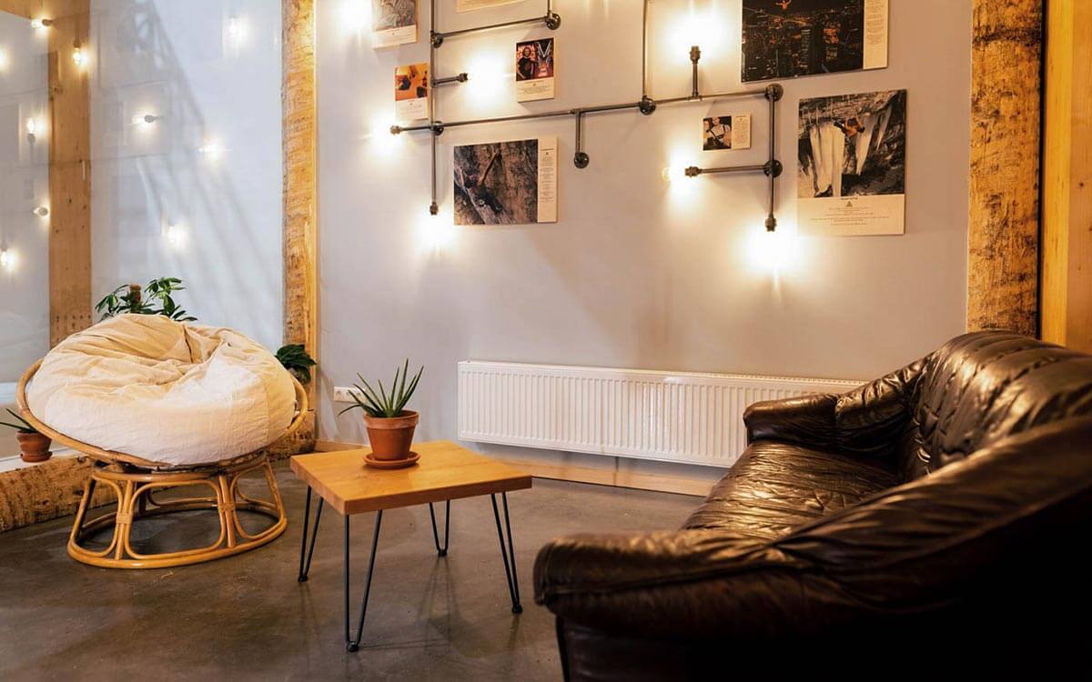 Bistrobereich mit gemütlichen Sitzmöglichkeiten wie einem Sitzsessel und einem braunen Ledersofa. An der Wand hängen Bilder von Bergkletterern. Auf dem kleinen Tischchen steht eine Sukkulente.