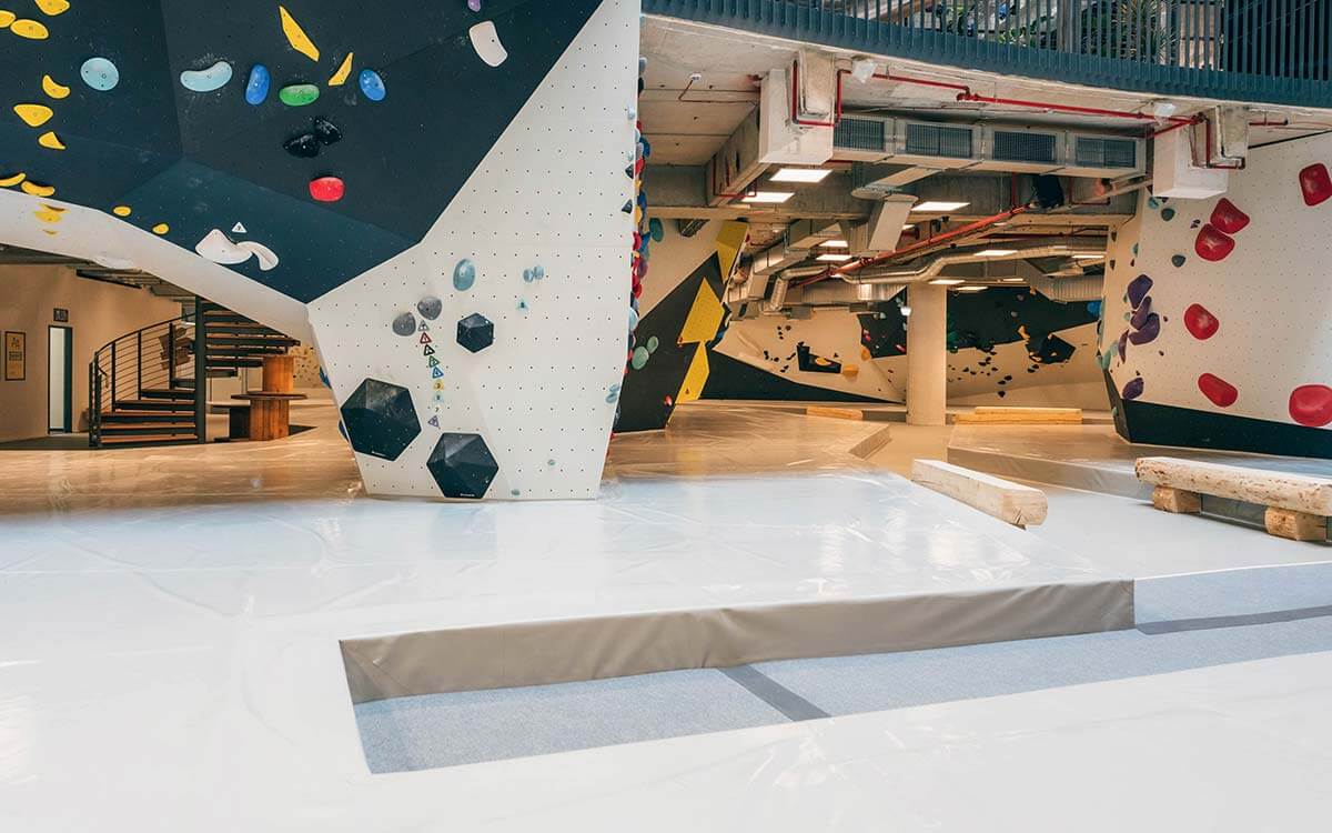 Weitläufiger Boulderbereich im Stuntwerk Troisdorf mit hellen Wänden, großen schwarzen und gelben Volumen und bunten Griffen. Offenes Hallendesign mit Loft-Charakter.