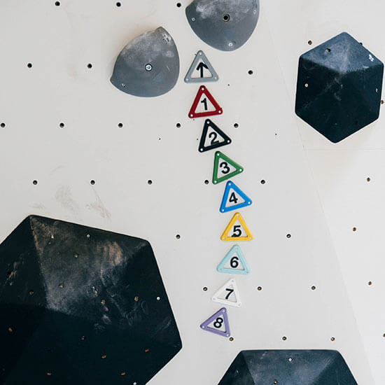 Weiße Boulderwand mit schwarzen Volumen und nummerierten, farbigen Dreiecken von 1 bis 8. Farbige Schwierigkeitsstufen zeigen die Level-Systematik im Stuntwerk.
