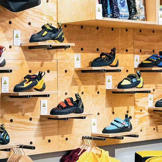 Verschiedene Boulder- und Kletterschuhe in kräftigen Farben an einer Holzwand präsentiert – perfekt für Einsteiger:innen und Profis.