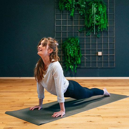 Frau führt im Yoga-Studio des Stuntwerks den heraufschauenden Hund aus. Der Raum ist hell, mit Holzfußboden und grüner Wanddekoration – Ausdruck von Energie und Leichtigkeit.