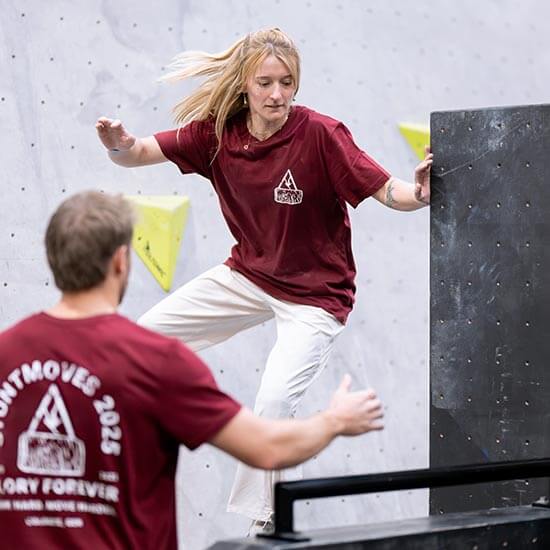 Zwei Teilnehmende trainieren gemeinsam Parkour im Stuntwerk. Eine Person überwindet ein Hindernis, während die andere unterstützt und auf die Technik achtet.