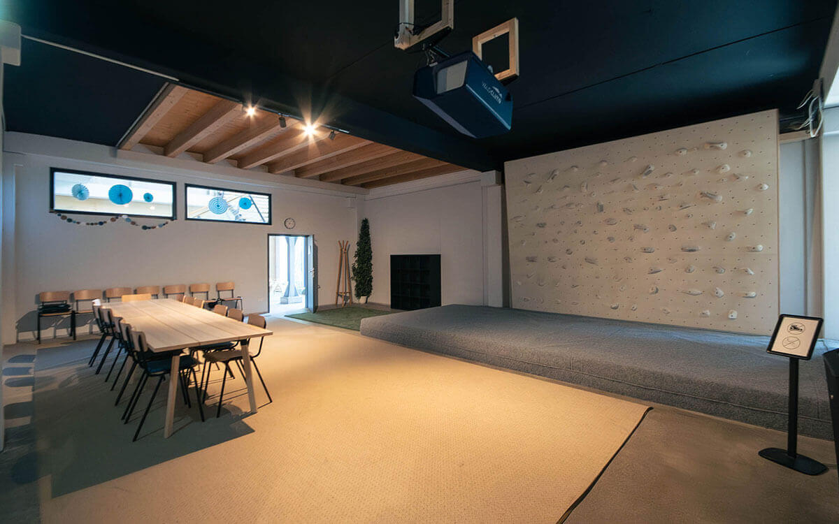 Freundlicher Kurs- & Kindergeburtstagsraum mit hellem Holztisch, vielen Stühlen, heller Kletterwand und Dekoelementen in Blau im Stuntwerk Trostberg.