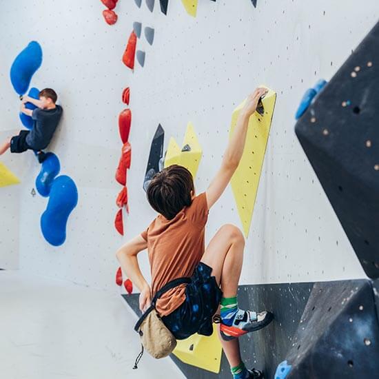 Zwei Jungs bouldern an einer Wand mit bunten Griffen im Stuntwerk. Konzentration, Bewegung und Spaß beim Kinderbouldern.