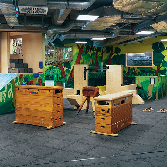 Heller Indoor-Kinderbereich mit Turngeräten, Holz-Kästen und farbenfroher Dschungelmalerei im Stuntwerk Troisdorf. Perfekt für Parkour- und Bewegungstraining für Kinder.