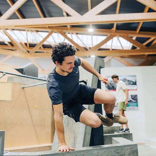 Athlet überquert geschickt ein Hindernis im Parkourbereich unter einem Dach aus Holzbalken