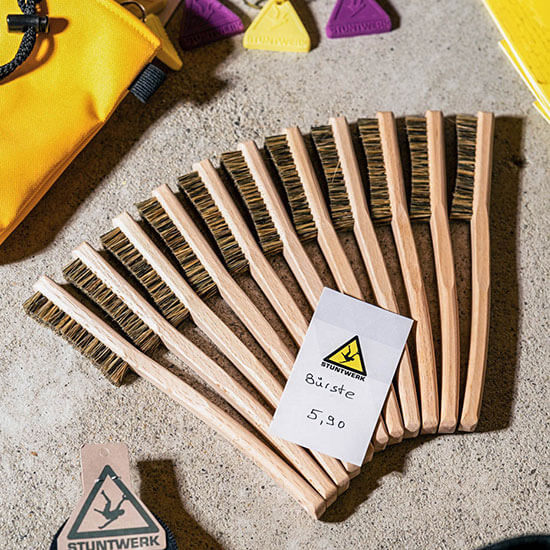 Holz-Boulderbürsten mit Stuntwerk-Logo liegen ordentlich arrangiert auf Betonboden – praktische Helfer beim Klettern.