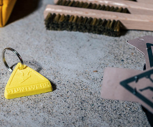 Gelber Stuntwerk-Schlüsselanhänger in Dreiecksform aus Chalk-ähnlichem Material – kleines, markantes Accessoire.