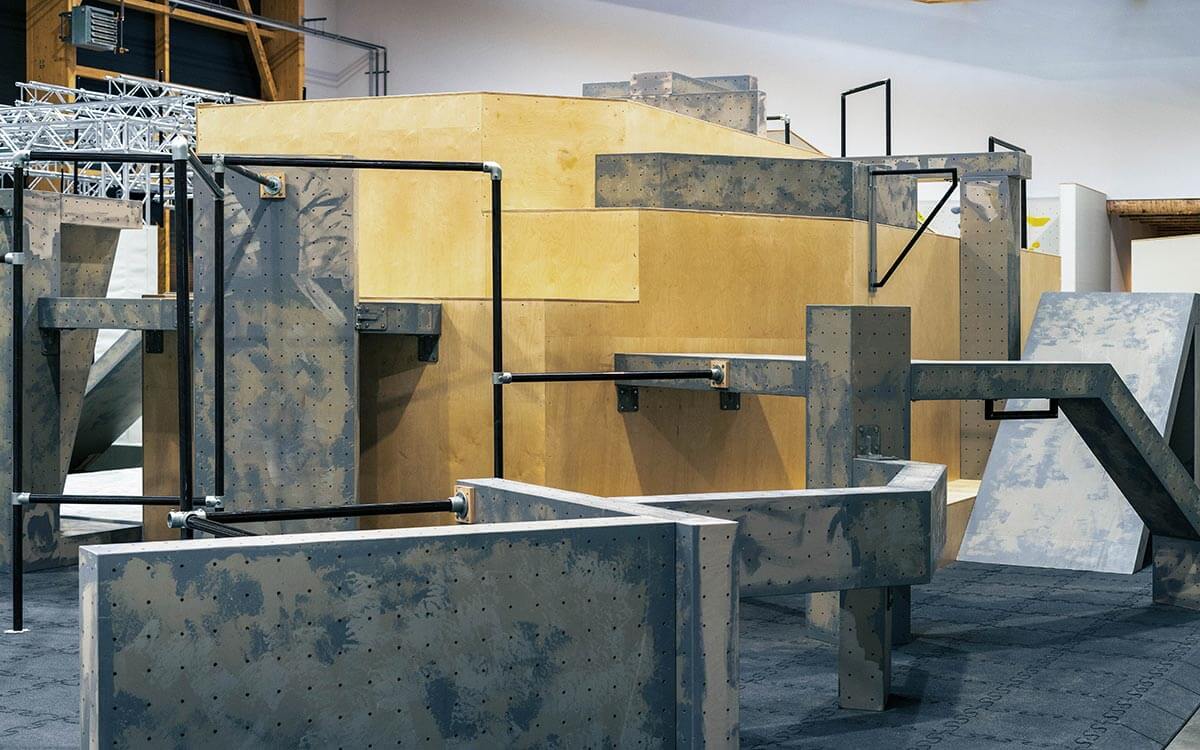 Parkourbereich - mit grauen, blockförmigen Hindernissen zum Springen und Klettern. Schwarze Stangen zum Hangeln und Schwingen.