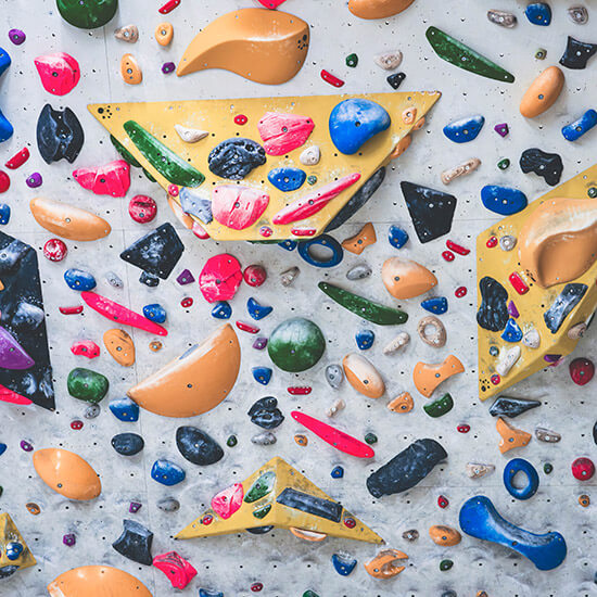 Bunte Boulderwand mit unzähligen Klettergriffen in Rot, Blau, Gelb, Grün und Schwarz auf hellgrauem Untergrund. Verschiedene Volumen und Formen für kreatives Klettertraining im Stuntwerk.
