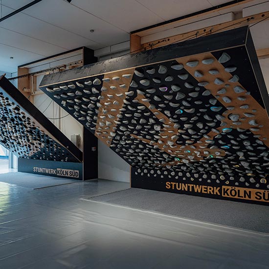 Zwei große Tensionboards mit schwarzen Holzflächen und weißen Klettergriffen im Stuntwerk Köln Süd. Die überhängenden Trainingswände sind symmetrisch angeordnet und dienen zum präzisen Technik- und Krafttraining beim Bouldern.