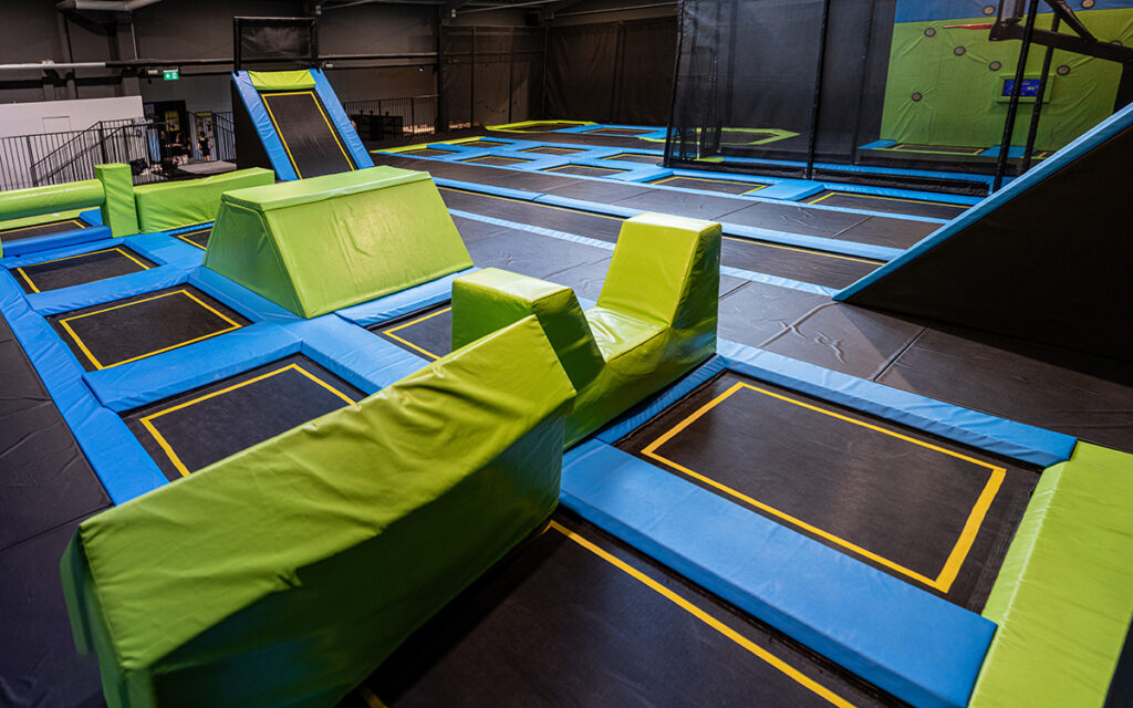 Weitläufiger Trampolinbereich mit verbundenen Sprungflächen, Schrägtrampolinen und gepolsterten Plattformen für Parkour- und Sprungtraining.