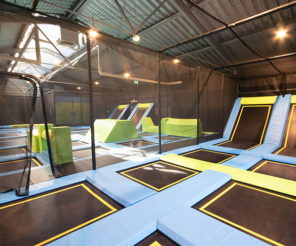 Große Indoor-Trampolinhalle mit blauen und gelben Sprungflächen, schwarzen Trampolinen und grünen Hindernissen im Stuntwerk Trostberg.