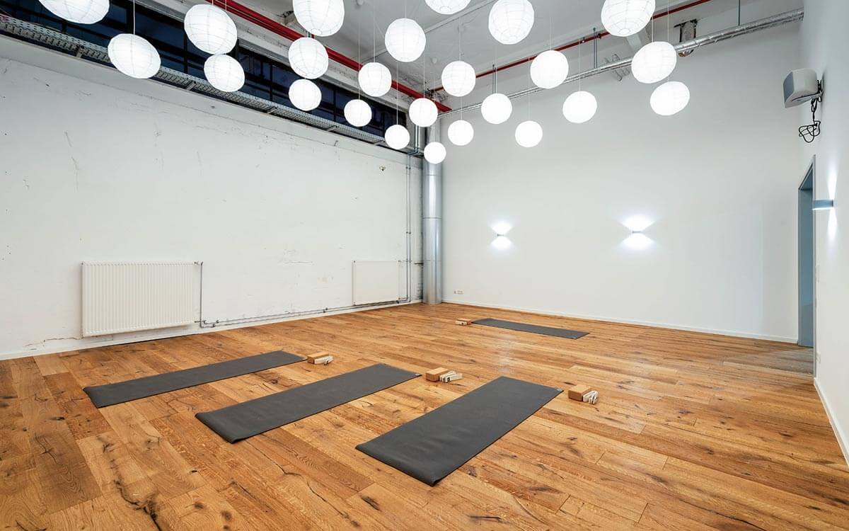 Heller Yogaraum im Stuntwerk mit Holzfußboden, Matten und stimmungsvollen Papierlampen.